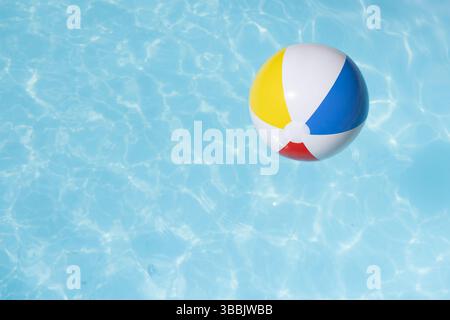 Inflatable beach ball floating on clear blue pool water, showing sunlit ripples and reflections Stock Photo