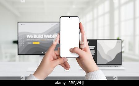 Smartphone mockup held in hands in office setting, with computer and laptop in background, ideal for corporate app design presentation Stock Photo