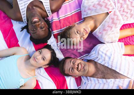 Posing diverse friends lying on pink striped towel in sunny park with child in tank top Stock Photo
