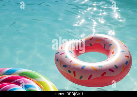 Pink donut-shaped inflatable ring floating in outdoor swimming pool, with sparkling turquoise water Stock Photo