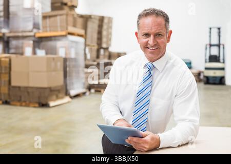 Tablet computer is resting on wooden crate inside warehouse, showing stacked cardboard boxes Stock Photo