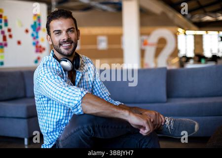 Sitting man wearing headphones on grey sofa in modern office near partition wall with question mark Stock Photo