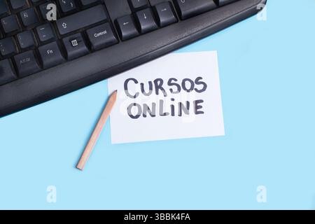 A black computer keyboard with a white paper note with cursos online phrase and a pencil on a light blue background Stock Photo