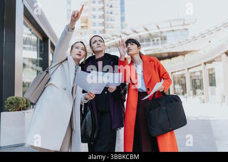 Three Businesswomen Collaborating Outdoors, Reviewing Papers, and Planning in an Urban Setting Stock Photo