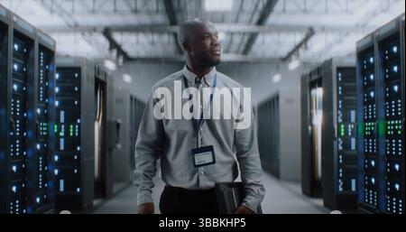 Big Data Center with Server Racks: Professional African American Specialist with Tablet Computer Walking In Warehouse. Internet Servers, Information Technology, Cyber Security and Telecommunications. Stock Photo