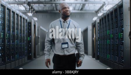 Big Data Center with Server Racks: Professional African American Specialist with Tablet Computer Walking In Warehouse. Internet Servers, Information Technology, Cyber Security and Telecommunications. Stock Photo