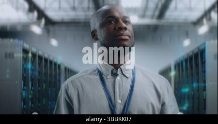 African American Administrator Walking in Futuristic Big Data Center with VFX, Smiling, Looking at Camera. Animated Diagrams of Internet Traffic on Servers. Information Technology and Digitalization. Stock Photo
