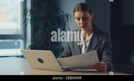 Business executive or manager in office reading a document with serious expression, sitting at desk with laptop. Concept of responsibility, analysis Stock Photo