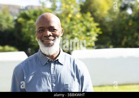 Senior African American man standing in garden, wearing light blue button-down shirt, smiling Stock Photo