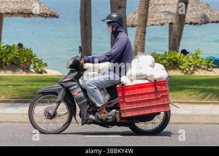 DANANG, VIETNAM, APR 24 2025, A motorbike loaded with plastic bags full or noodle rides along the city beach Stock Photo