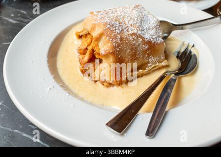 Apple strudel with vanilla custard sauce on a plate with two sets of utensils Stock Photo