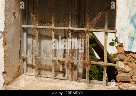 Old derelict roofless house. Rusty grill on a window and broken shutters behind. Stock Photo