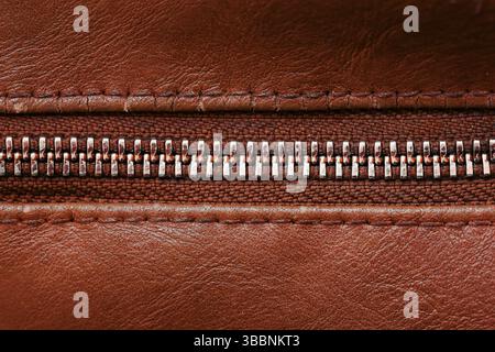 Brown leather zipper texture. Closeup of metallic zip on leather surface. High-quality fashion detail. Horizontal design element. Macro metal teeth. Stock Photo