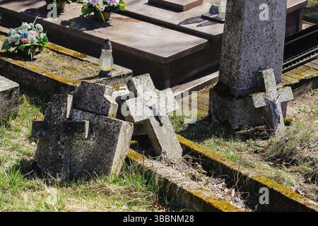 Old cemetery with broken tombstones. Fallen stone crosses on graves. Forgotten gravesite with moss and grass. Historic graveyard in decay. Stock Photo
