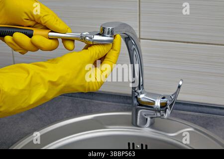 plumber in yellow rubber gloves repairing and servicing a water faucet in a kitchen Stock Photo