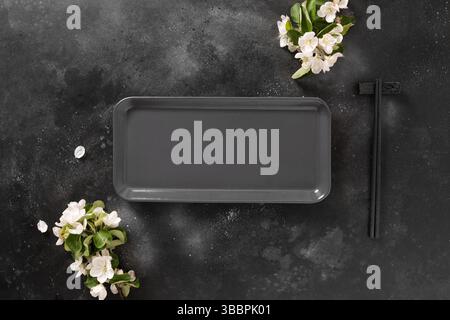 Empty rectangular plate for asian food with black chopsticks on black background with spring blossom white flowers. Asian style. View from above. Copy Stock Photo