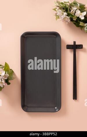 Empty rectangular gray plate for asian food with black chopsticks on pink background surface with spring branches. Asian style. View from above. Verti Stock Photo