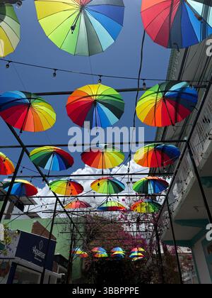 Colorful umbrellas create a joyful canopy against a bright blue sky in a vibrant urban street art installation Stock Photo