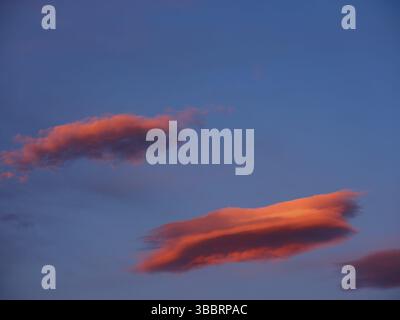 Red-coloured cumulus cloud and lenticularis cloud in the blue evening sky Stock Photo