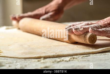 Person preparing a dough with a rolling pin. Female hands roll out a dough with a rolling pin. Closeup of man rolling dough with rolling pin for Stock Photo