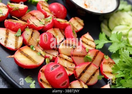Grilled radishes with cucumber slices and sour cream sauce served on a dark grey plate, close-up, dutch angle view,  real photo, not AI generated Stock Photo