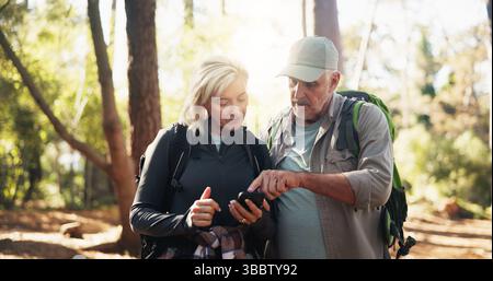 Directions, map and phone with old couple in forest together to search for destination. App, lost and pointing at mobile with senior people outdoor in Stock Photo