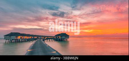 Amazing sunset over water villas and bungalows in Maldives tropical island paradise, stunning seascape luxury resort vacation destination. Wooden pier Stock Photo