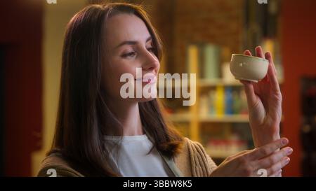 Female potter artist designer sculptor Caucasian woman girl smiling artisan saleswoman owner in pottery workshop looking at handmade cup clay ceramics Stock Photo