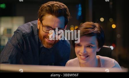 Caucasian businesswoman businessman together working computer in night office smiling business woman man cooperation high five gesture teamwork co Stock Photo
