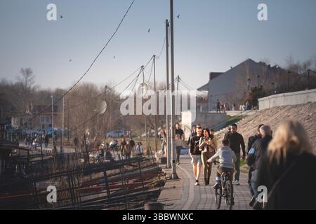 PANCEVO, SERBIA - MARCH 3, 2025: Late-afternoon scene on the Tamis river promenade in Pancevo, Serbia: a young couple walks hand-in-hand while cyclist Stock Photo