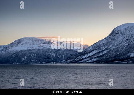 Calm Norwegian sea and mountains covered by thin layer of snow in the autumn. Colorful clouds during sunrise. Harstad, Norway. Stock Photo