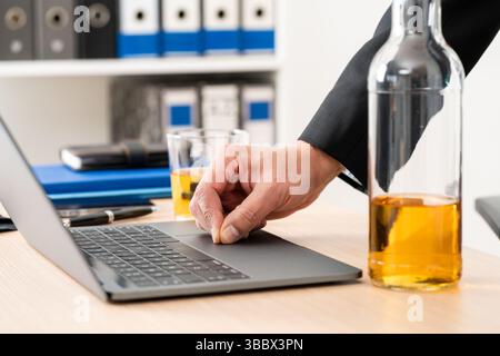Close-up of entrepreneur hands drinking alcohol working on laptop at homeoffice Stock Photo