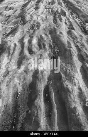 Icy Trail with Frost Patterns, Footprints and Tire Tracks – Monochrome Winter Texture Stock Photo