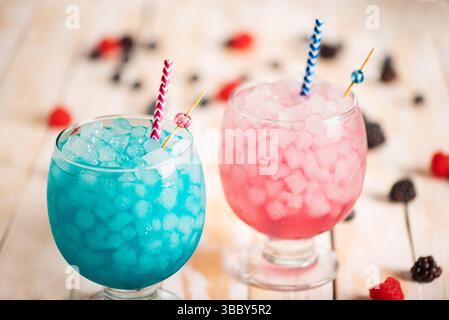 Glasses with ice filled with raspberry and blackberry soda with blueberries, on a white wooden table. Stock Photo
