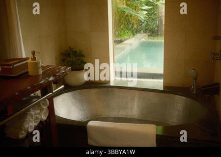 Tranquil bathroom featuring a copper bathtub with a view of the pool through a large window Stock Photo