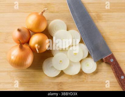 chopped syellow onion on a wooden cutting board, top view. Whole yellow onions and a knife on a cutting board, top view. Stock Photo