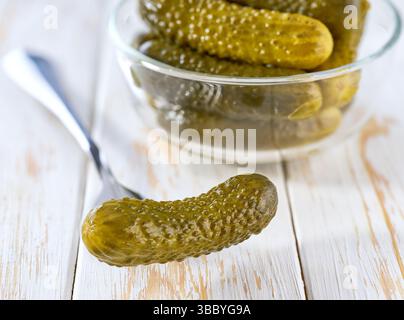 pickled cucumbers in a transparent glass bowl on a white wooden table, selective focus. tasty fermented cucumbers in a clear glass bowl on a white tab Stock Photo