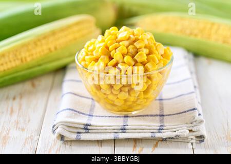 Transparent bowl with canned food maize on a light kitchen table, selective focus. Stock Photo