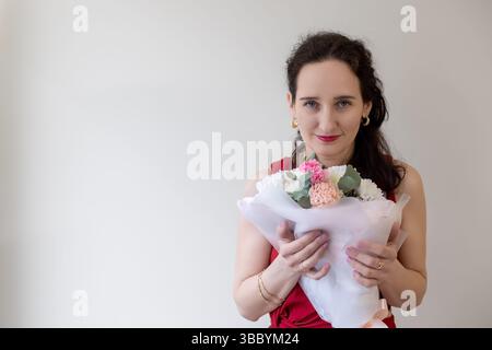 Woman in a red dress holding a bouquet of flowers, elegant and joyful moment with soft colors. Space for text. Stock Photo