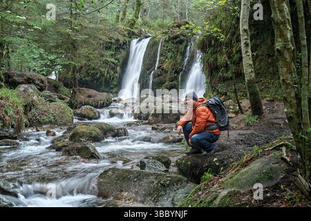 Man embraces the wild beauty of Glenmalure, facing the waterfall and stream deep in the Irish wilderness. Stock Photo