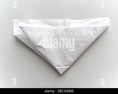 A white paper is folded into a triangle. The paper is white and has a pattern on it Stock Photo