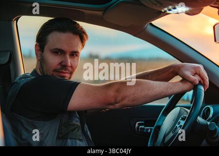 Handsome young man driving car at sunset Stock Photo
