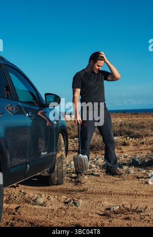 Frustrated man with shovel stands near his car stuck in the sand Stock Photo