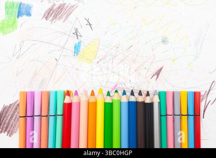 Multi-colored pencils lie on white paper drawn with multi-colored curved lines. Stock Photo