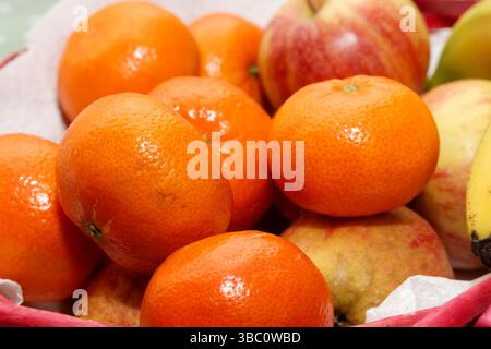 Closeup image of a colorful assortment of fresh fruits including juicy oranges, red apples, and a banana placed together in a basket Stock Photo