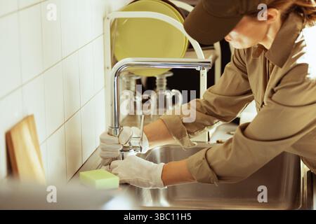 A plumber installs a chrome faucet in a kitchen sink, wearing gloves. The scene suggests focused home repair and skilled plumbing work. Stock Photo