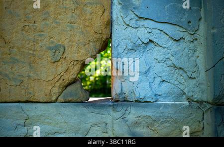 Close-up of a weathered stone wall with a narrow gap revealing lush greenery behind, evoking mystery and contrast. Stock Photo