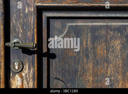 Close-up of a weathered chapel door with vintage handle and keyhole, showing rich texture and patina in natural light. Stock Photo