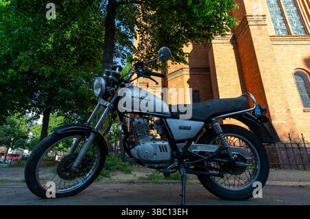 Classic Suzuki GN125 parked on a Berlin street with a historic red brick church in the background, summer afternoon light. Stock Photo