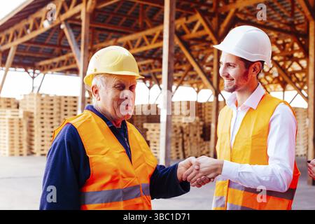 Portrait of young construction company manager thanks and shaking hands with confident senior foreman. Being thankful to colleague for many years of g Stock Photo